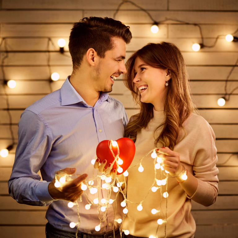 happy couple facing each other, smiling, both holding a string of lights